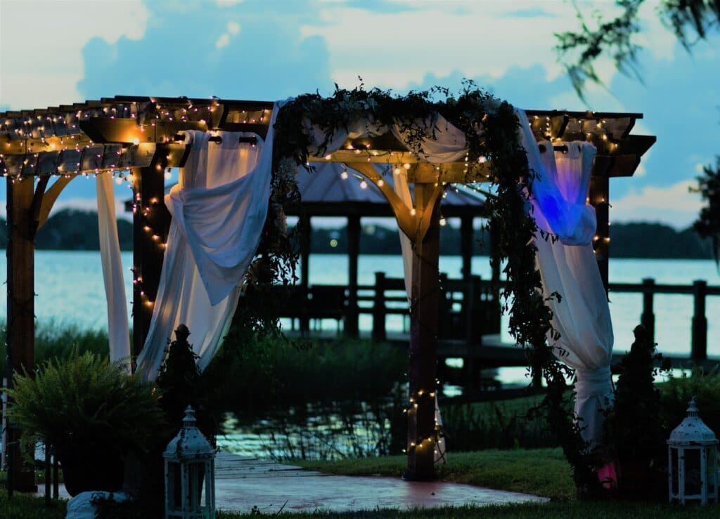 outdoor wedding ceremony area decorated with white linens, green vines, and beautiful lights